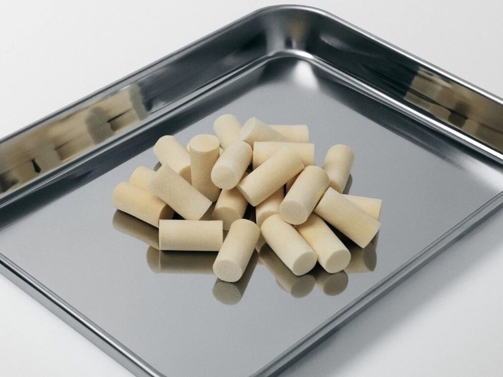 A batch of cream-colored mycelium earplugs scattered on a stainless steel medical-grade tray.