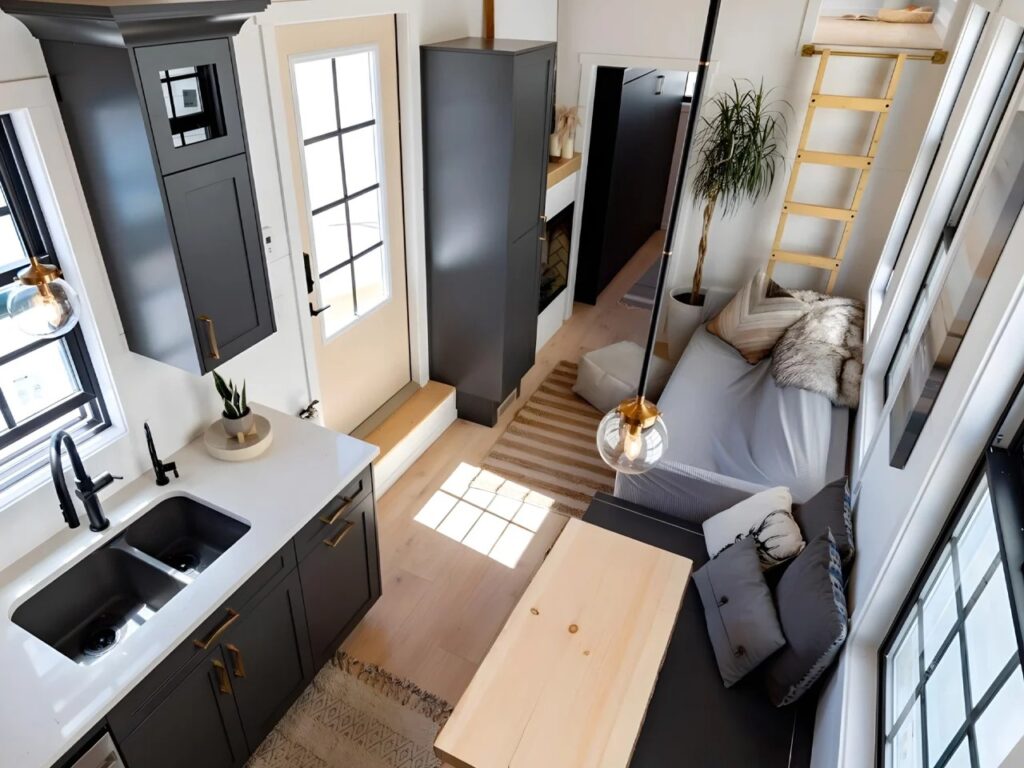 High-angle interior view of Harmony tiny home living room with a gray sofa, wooden stairs, and dark grey cabinetry.
