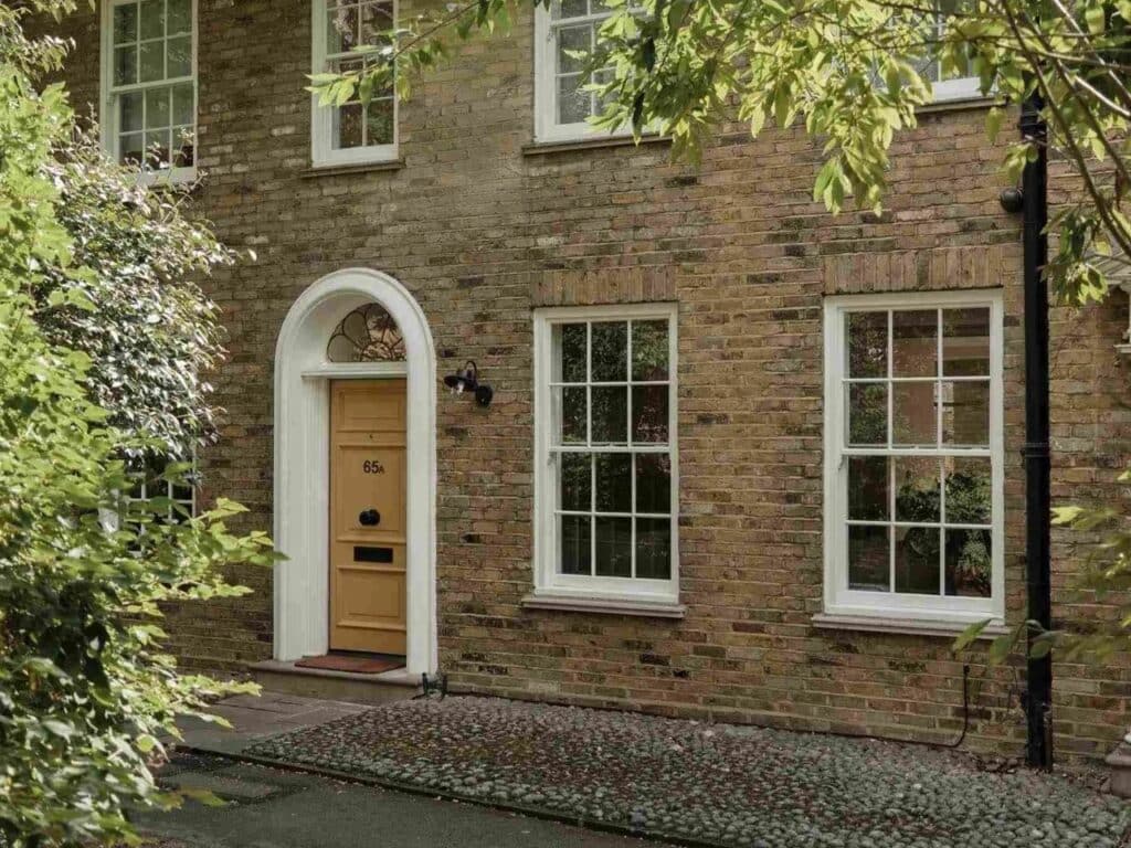 Traditional Georgian brick facade of House 65A in Islington with a yellow arched front door and sash windows.