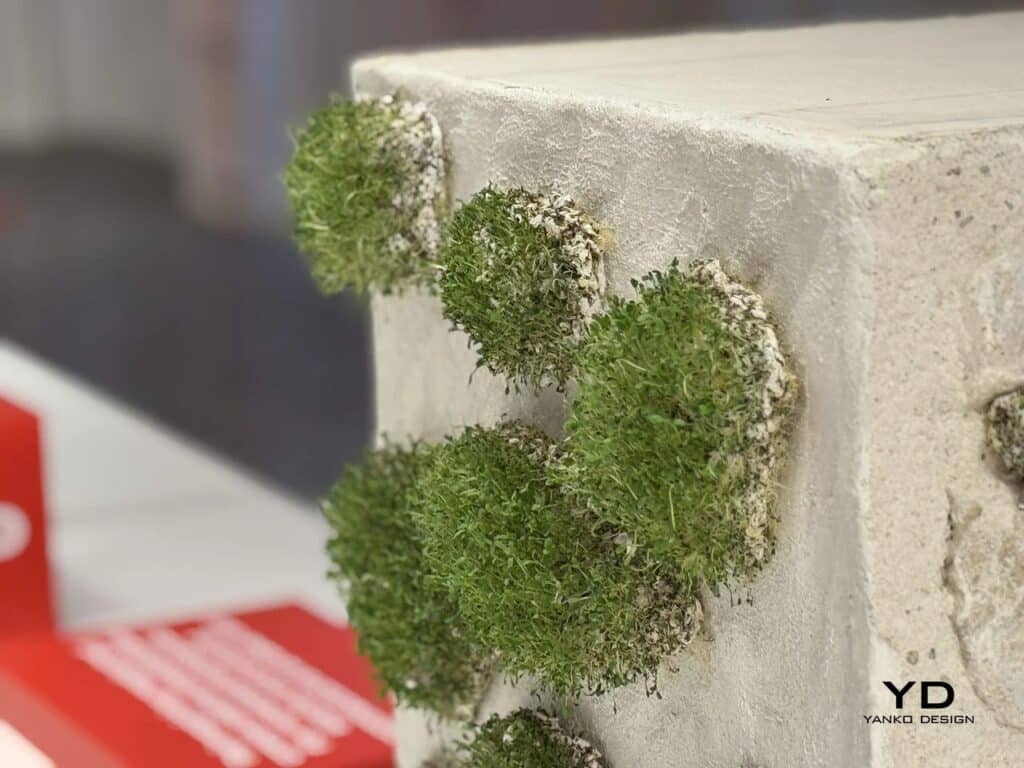 Side profile of circular green bio-units emerging from a light-colored wall surface.