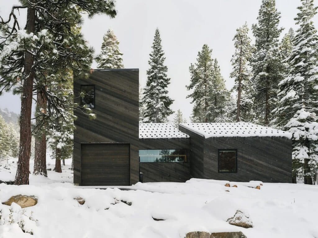 Front facade of Staggered Cabin showing metal roofs with snow guards and dark wood siding amidst snow.
