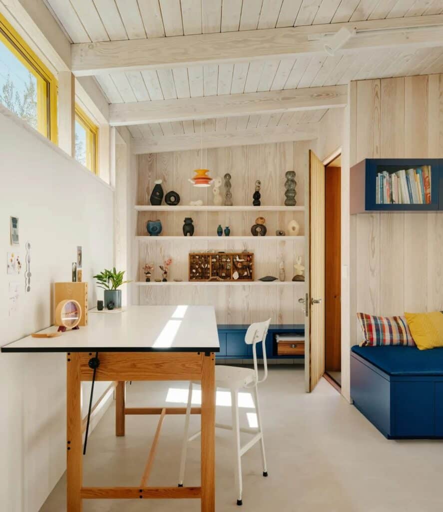 Minimalist interior of Two-Fold Studio featuring a white work table, blue storage bench, and ceramic display shelves.