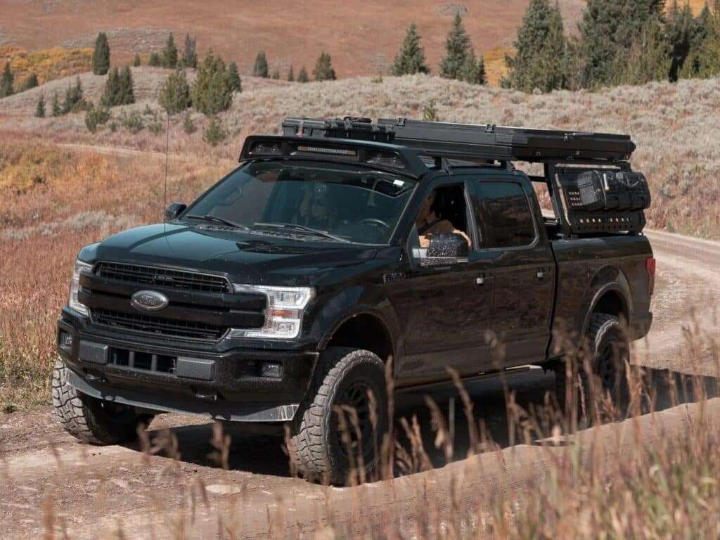 Black pickup truck driving on a dirt road with a folded Altus hardwall rooftop cabin in its low-profile transport mode.