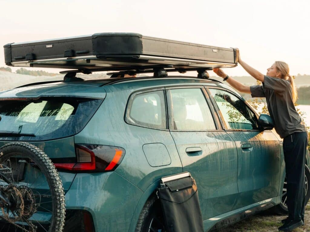 A woman closing the Thule Widesky hardshell rooftop tent on a green SUV, showing its compact profile.