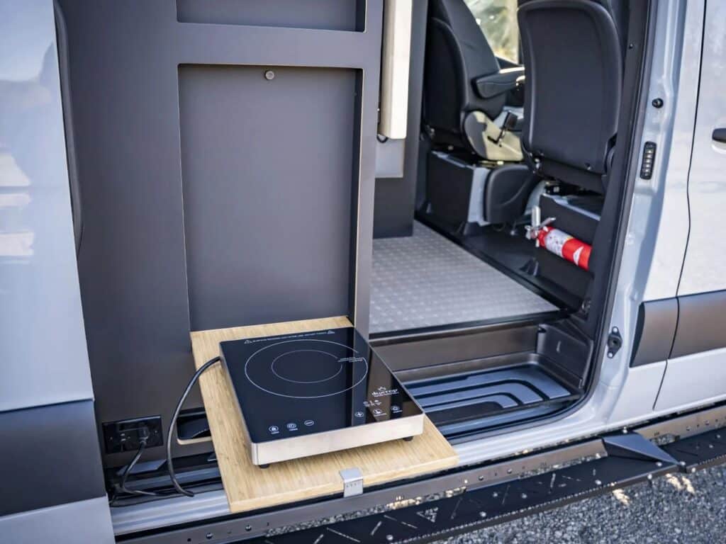 A portable induction cooktop placed on the fold-out bamboo table at the van's side entrance.