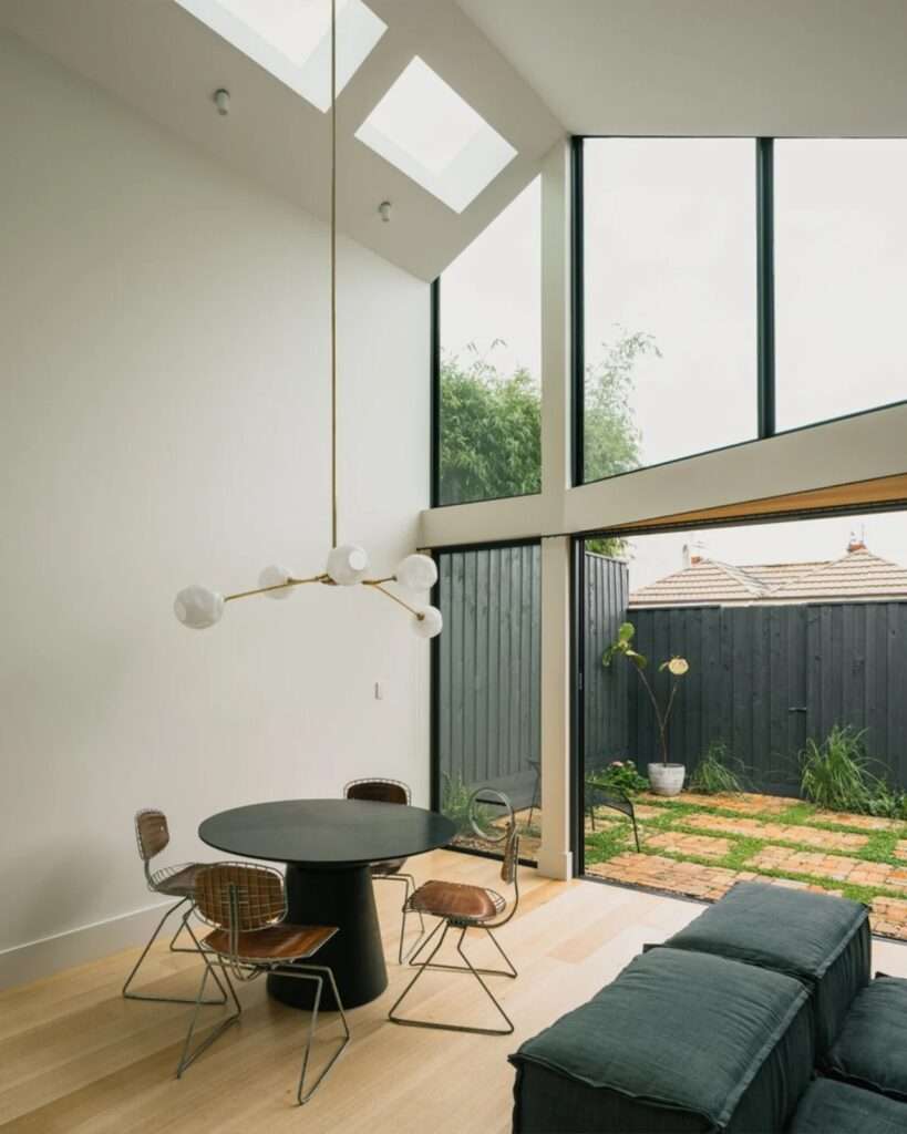 Bright interior dining area with high ceilings, a minimalist pendant light, and a large glass wall framing a private courtyard.