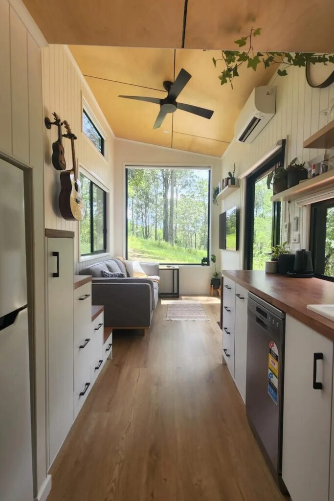 Interior view looking towards the living room with a ceiling fan, light wood floors, and large windows.