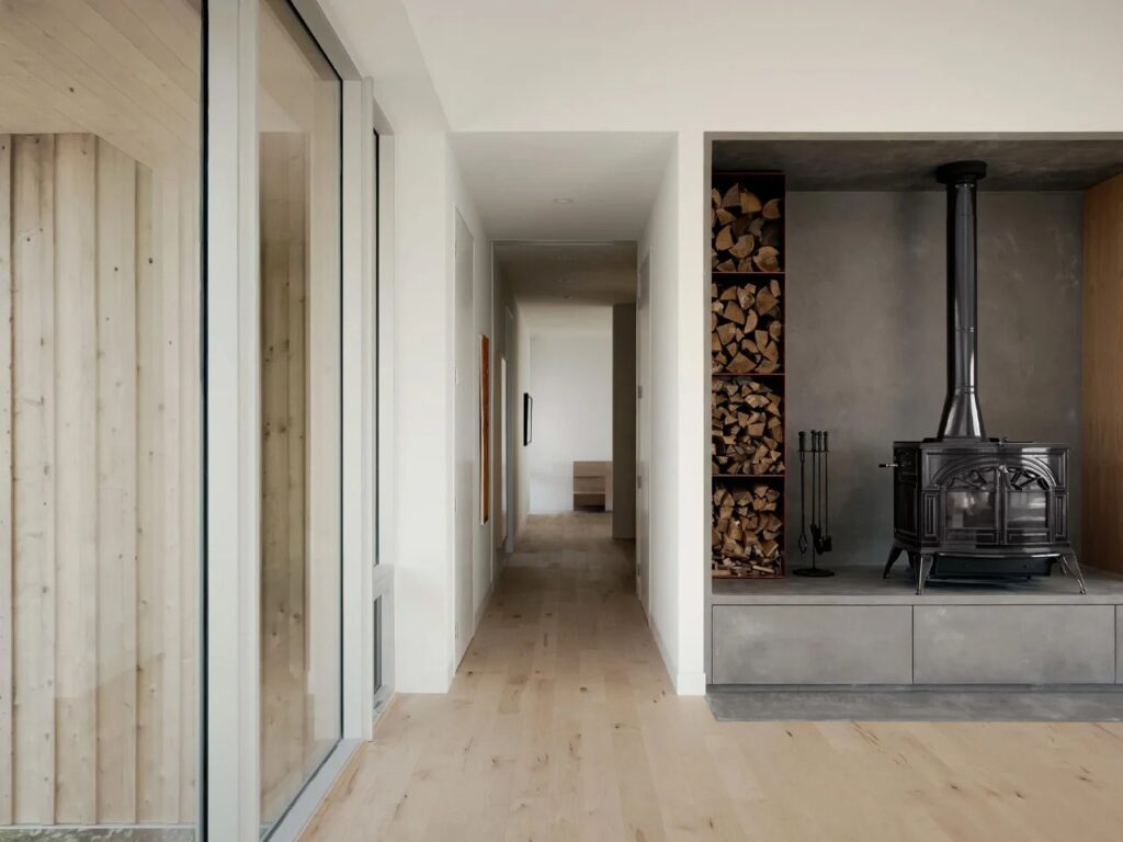 Modern minimalist interior of East River Residence featuring a wood-burning stove, concrete hearth, and light wood flooring.