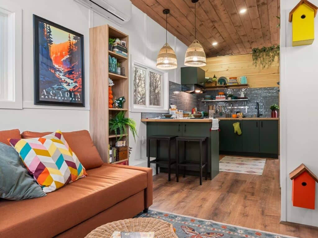 Interior view of a tiny home showing a green kitchen island, wooden ceilings, and a cozy living area with a brown couch.
