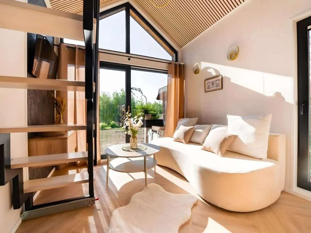 Interior of Lox tiny home living room with a curved cream sofa, large glass doors, and wooden slatted ceiling.