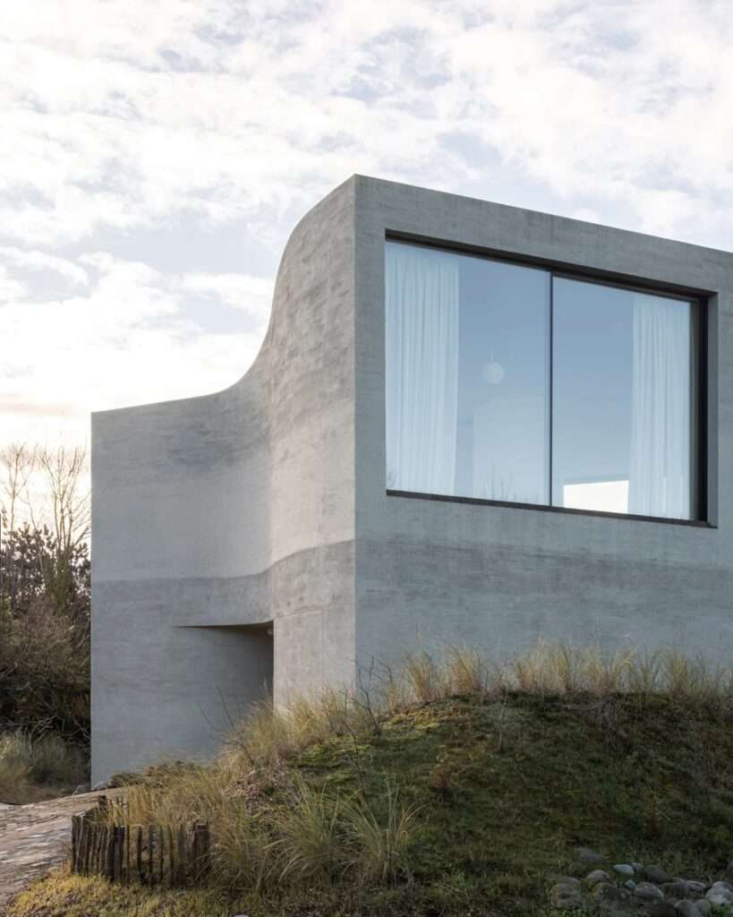 Close-up of the textured concrete facade and a large window reflecting the sky at Villa Nouvelle Vague.