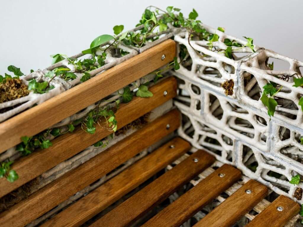 Close-up detail of the PhytoSymbiosis bench showing the juxtaposition of wooden seating slats against the porous bio-concrete structure with English Ivy growth.