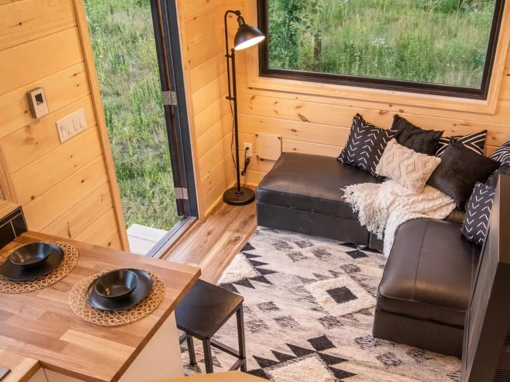 Interior living room of Scandi Inn with pine tongue-and-groove walls, a dark L-shaped sofa, and a large window.