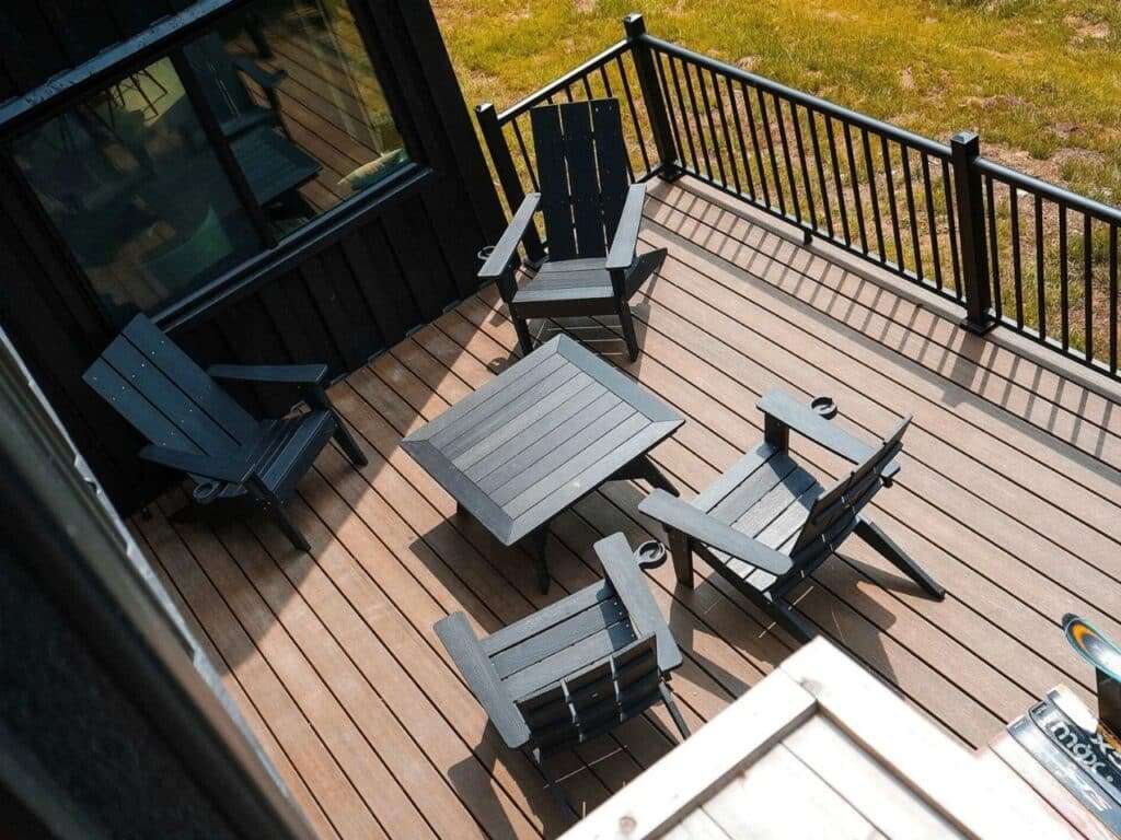 Top-down view of the upper wooden terrace of Fairmont Villa featuring modern black Adirondack chairs and a table.