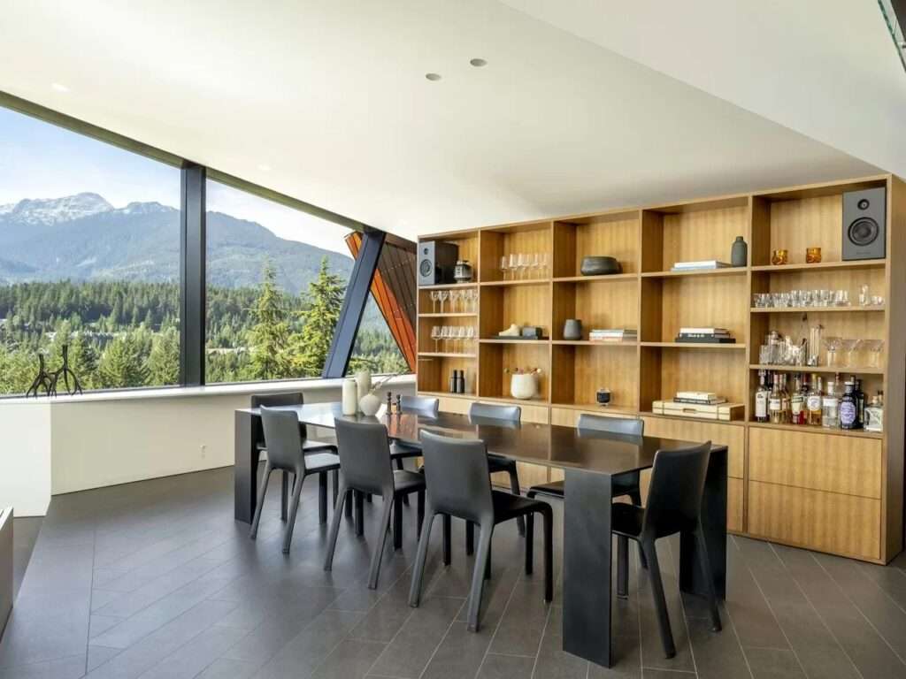 Modern dining room in Hadaway House with a long black table, wooden shelving unit, and panoramic mountain views through slanted windows.