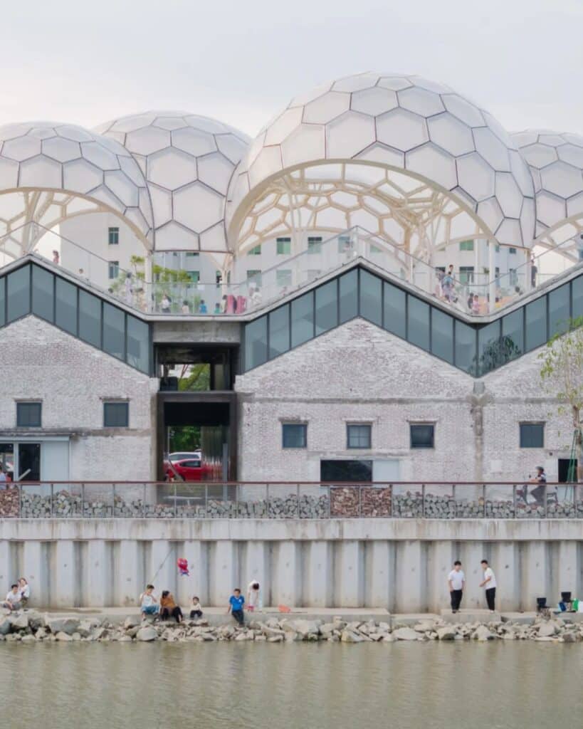 Waterfront facade of Yongping Warehouse in Foshan showing the original brick walls and the new zigzag roofline with glass sections.
