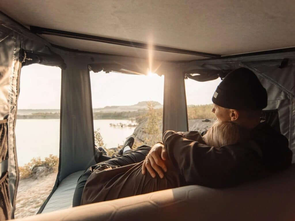 Interior view of Thule Widesky tent with a couple reclining against the integrated sofa feature overlooking a lake at sunset.