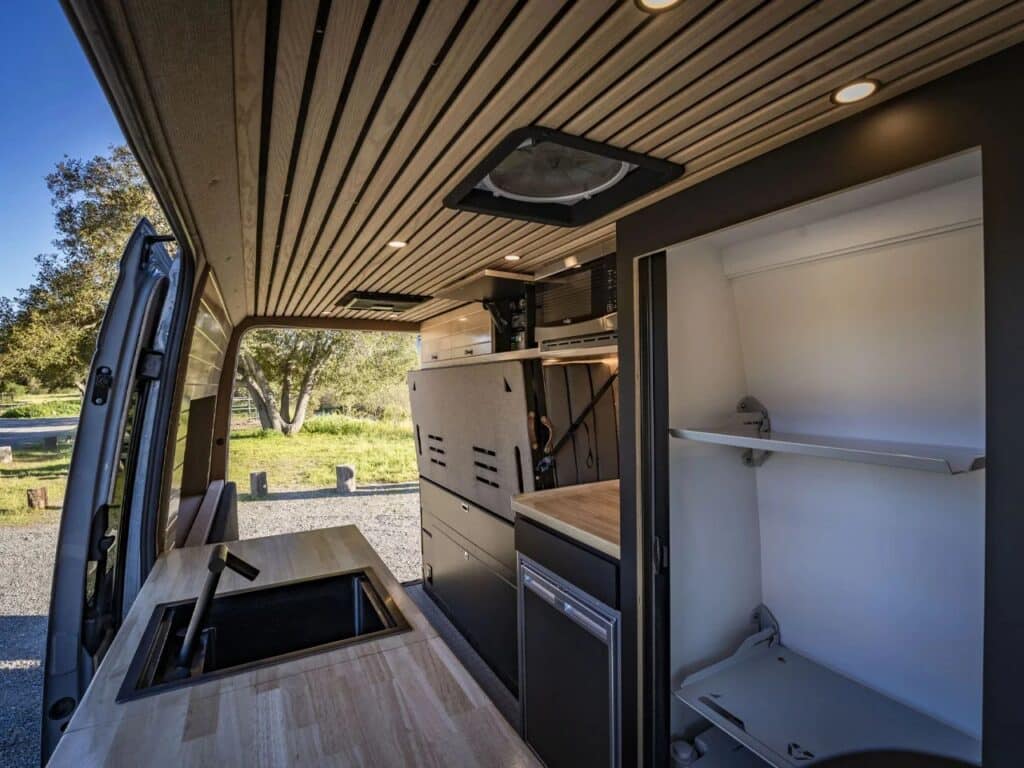 Wide interior view showing the wooden slat ceiling, kitchen counter with sink, and the folded Murphy bed on the side wall.