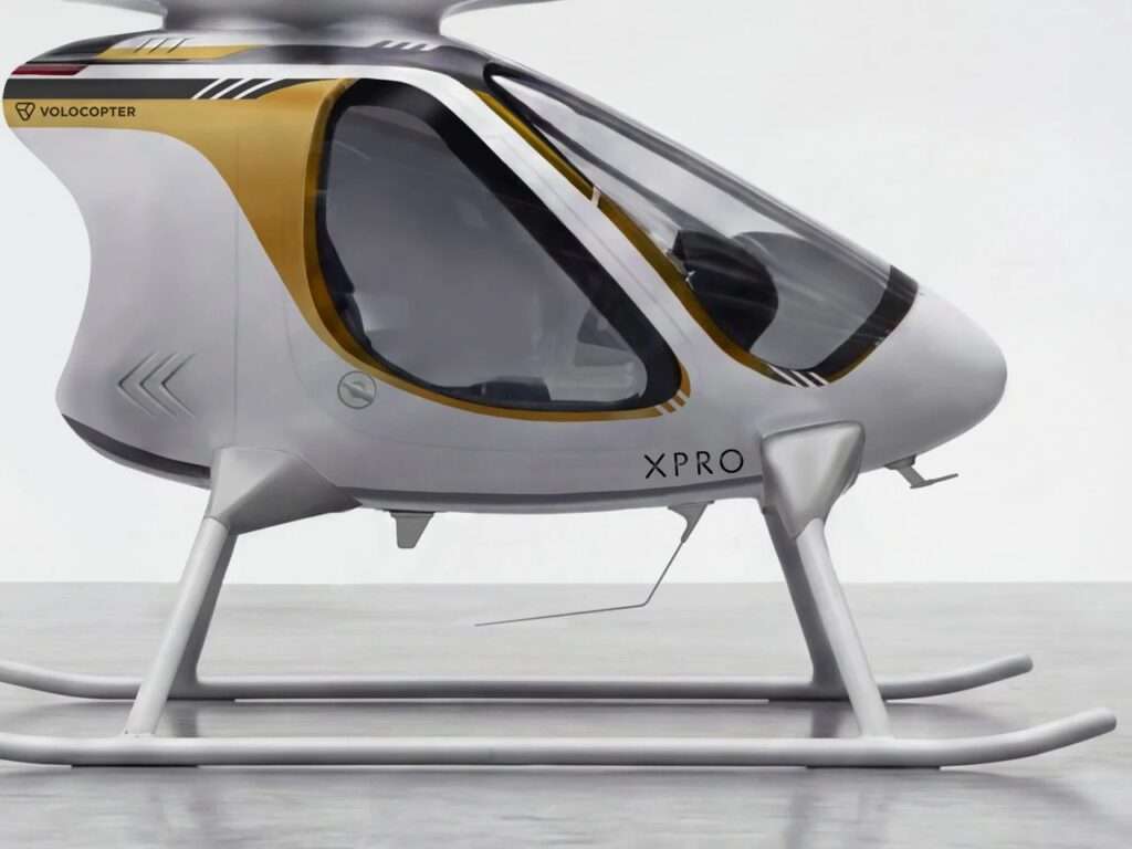A medium profile shot focusing on the central fuselage and cabin section of the Volocopter VoloXPro, highlighting the gold trim and the 'XPRO' designation against the white body.