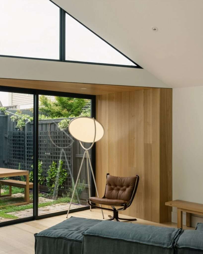Interior detail of a living area featuring timber wall paneling, a leather lounge chair, and a view of a black timber fence in the garden.