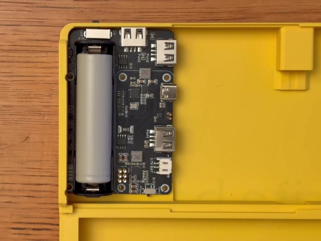 Close-up of the internal power management board and 18650 battery holder inside the yellow 3D printed base.