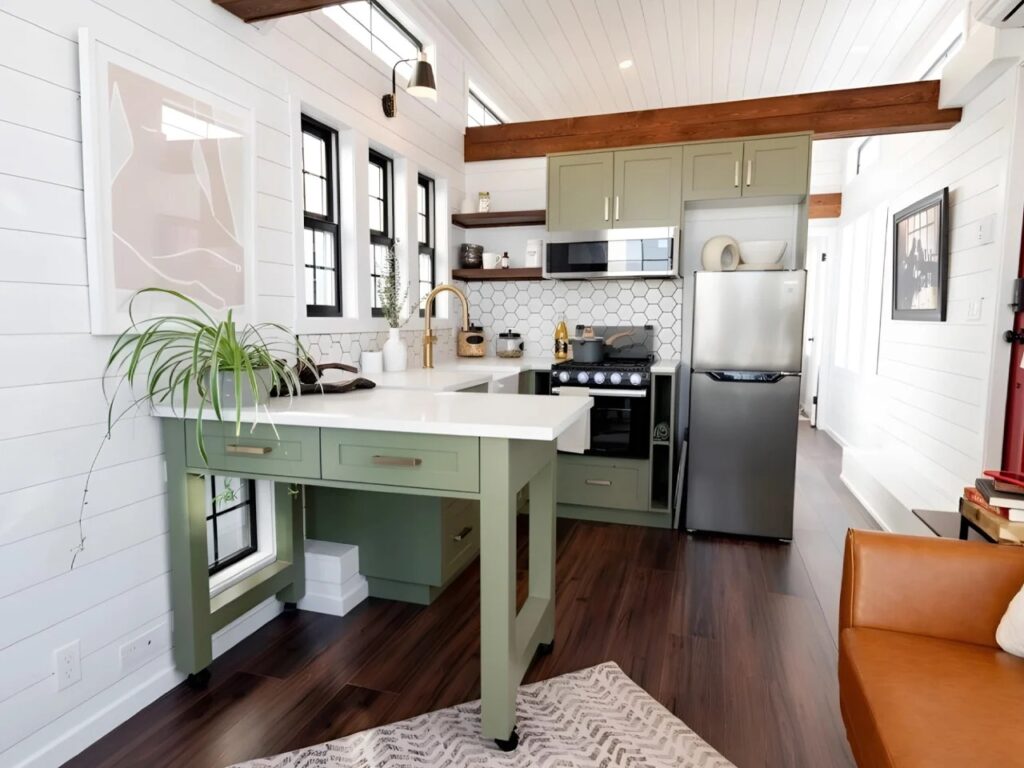 Contemporary kitchen in Daphne tiny house featuring sage green cabinets, white countertops, and a subway tile backsplash.