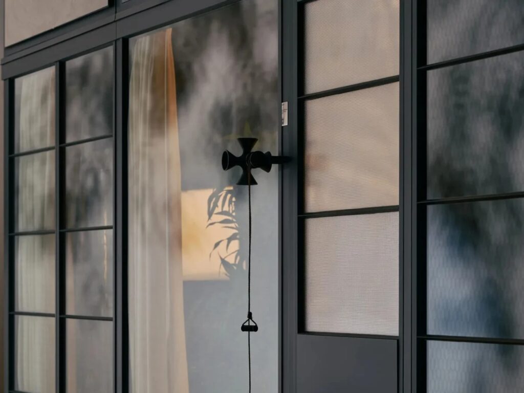 Detail of an Eames Pavilion glass door with a cruciform black handle and textured glass panels.