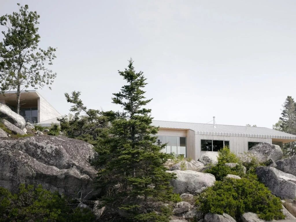 Low-angle shot of East River Residence partially hidden behind evergreen trees and large granite boulders in Nova Scotia.