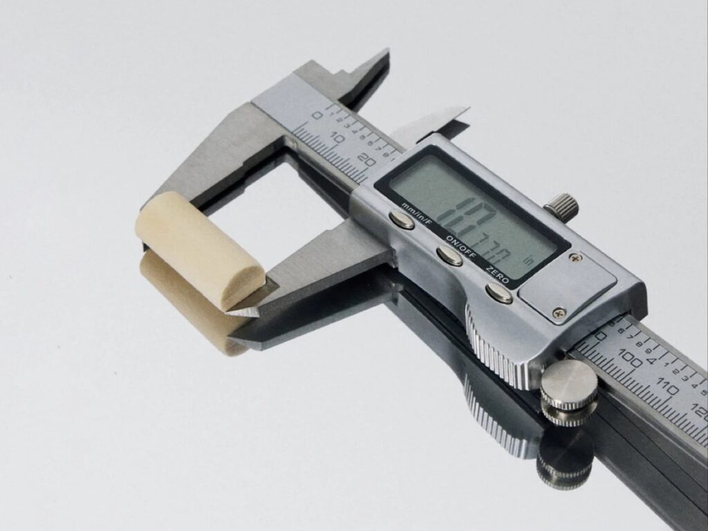 Digital caliper measuring the precise diameter of a GOB mycelium earplug on a reflective surface.