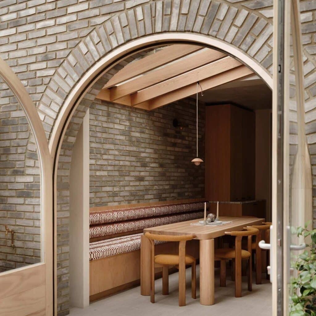 Close-up of a structural brick arch framing a modern dining area with Douglas fir ceiling beams and a built-in wooden bench.