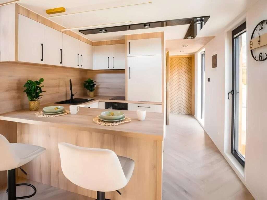 Modern compact kitchen in Lox tiny home with light wood cabinets, white upper units, and a breakfast bar.