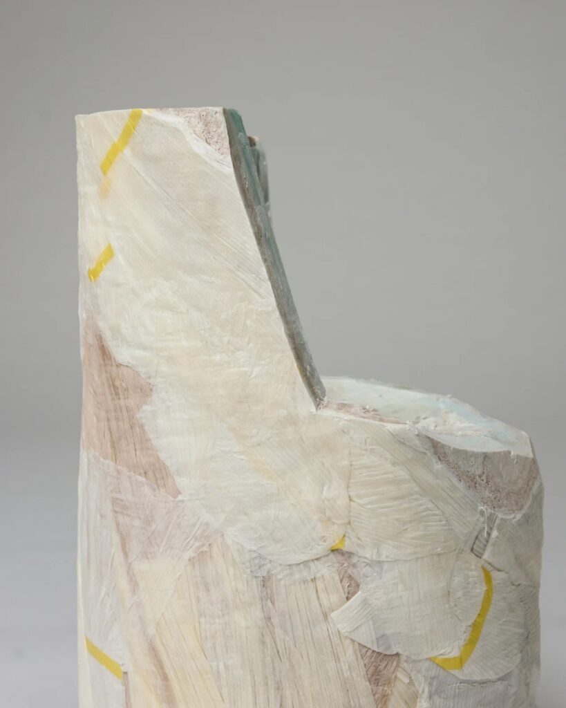 Side profile detail of a carved paper chair showing the layered construction and yellow marking tape.