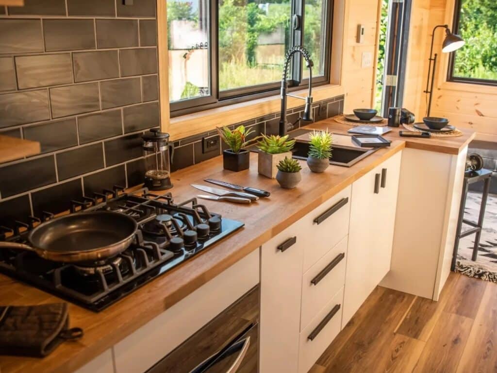 Modern tiny house kitchen in Scandi Inn with butcher block countertops, white cabinetry, and black tile backsplash.