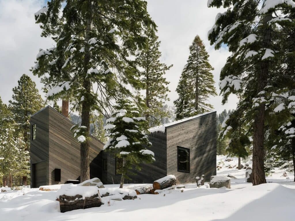 Modern mountain cabin with multiple staggered volumes and slanted roofs integrated into a sloped forest site.