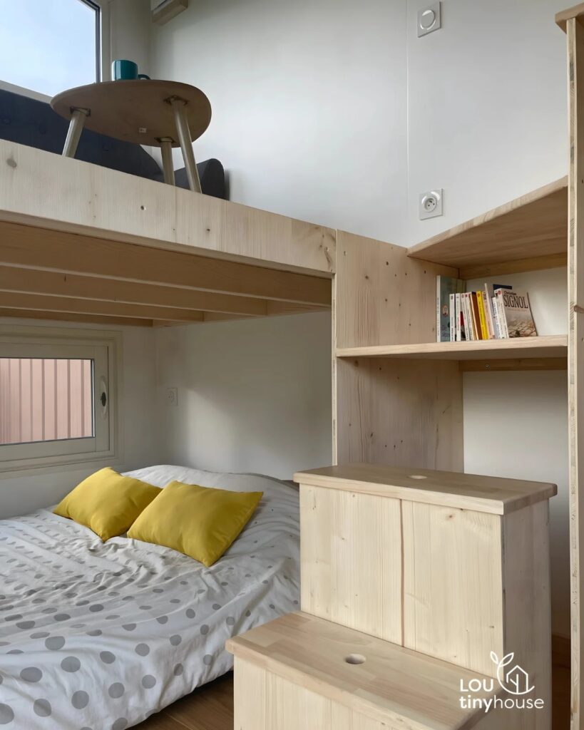 Ground floor bedroom with a double bed and wooden storage stairs in a tiny house.