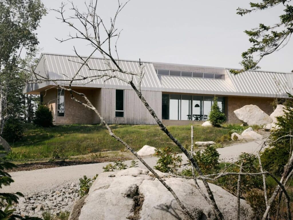 Exterior view of East River Residence showing the metal roofline and wooden cladding integrated with the grassy and rocky slope.