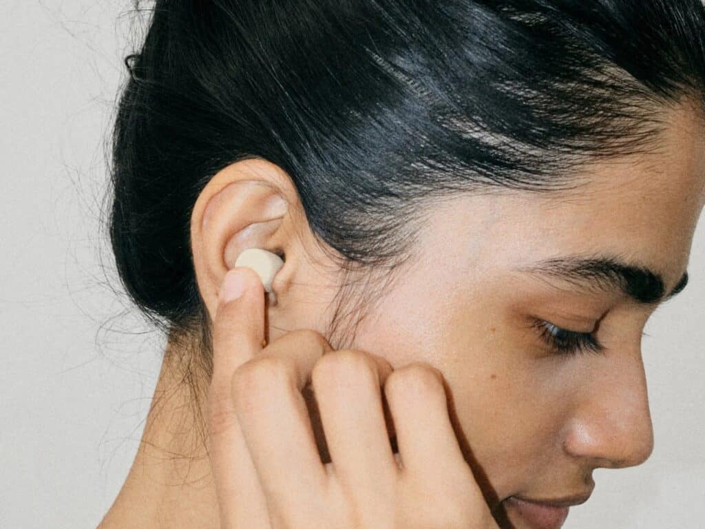 Close-up of a person inserting a soft mycelium earplug into the ear canal for sound protection.