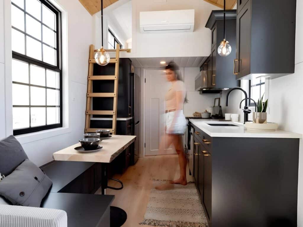 Full-size kitchen in Harmony tiny home with dark cabinets, white countertops, and a built-in dining bench.