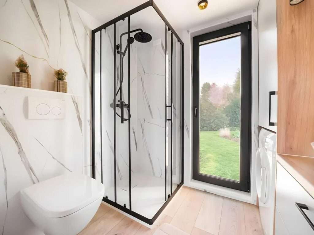 Contemporary bathroom in a tiny house with marble-finish walls, a glass shower cabin, and a large window.