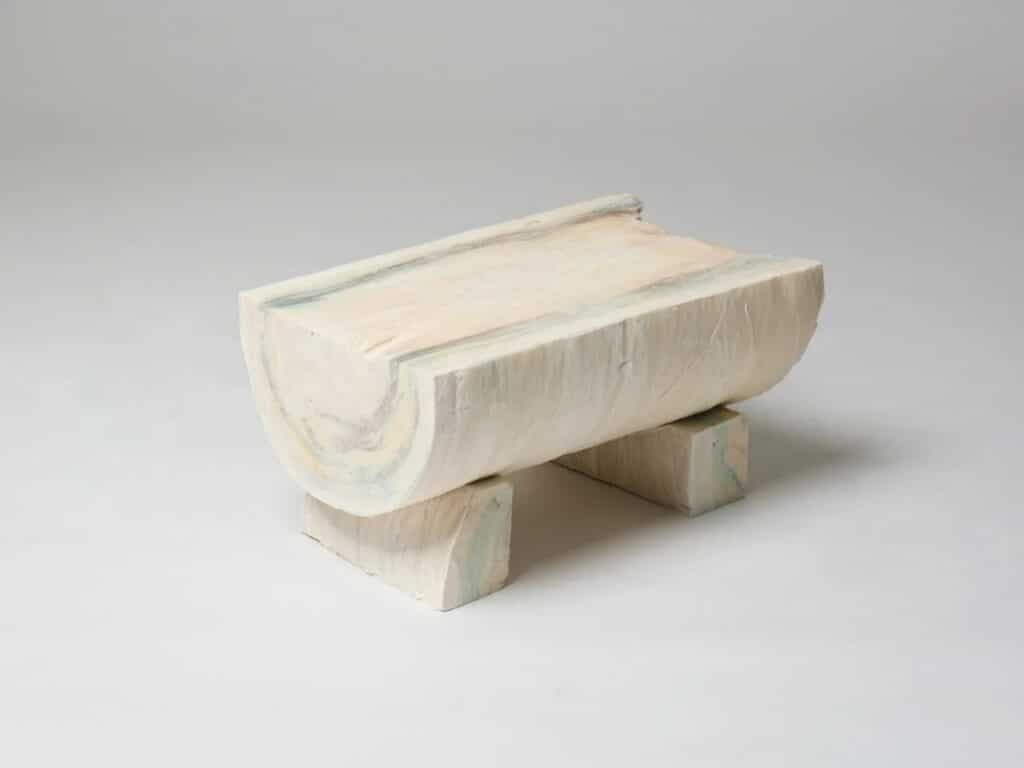 A low bench or coffee table made from a halved horizontal paper log resting on two rectangular blocks.