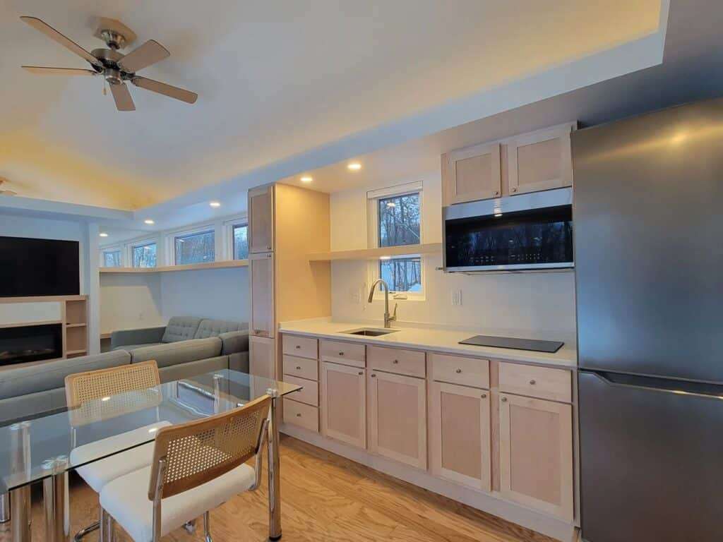 Modern compact kitchen in Shoreline House featuring light wood cabinetry and full-size stainless steel appliances.