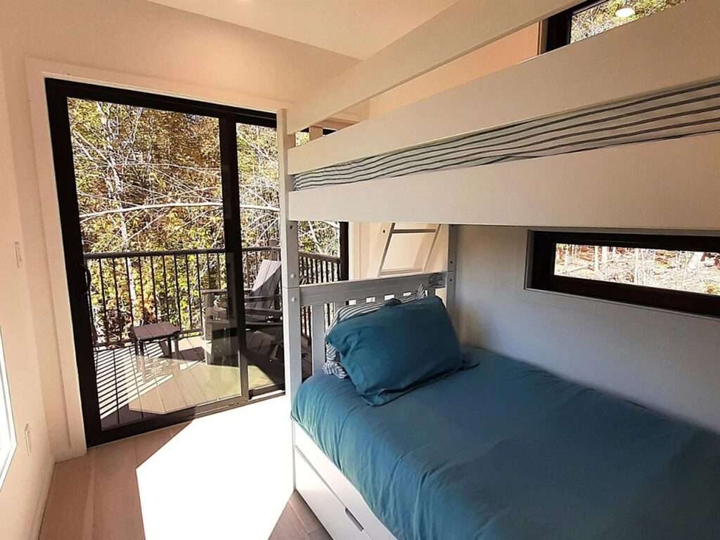 Minimalist interior bedroom in a container home with white bunk beds and a glass door leading to a balcony.