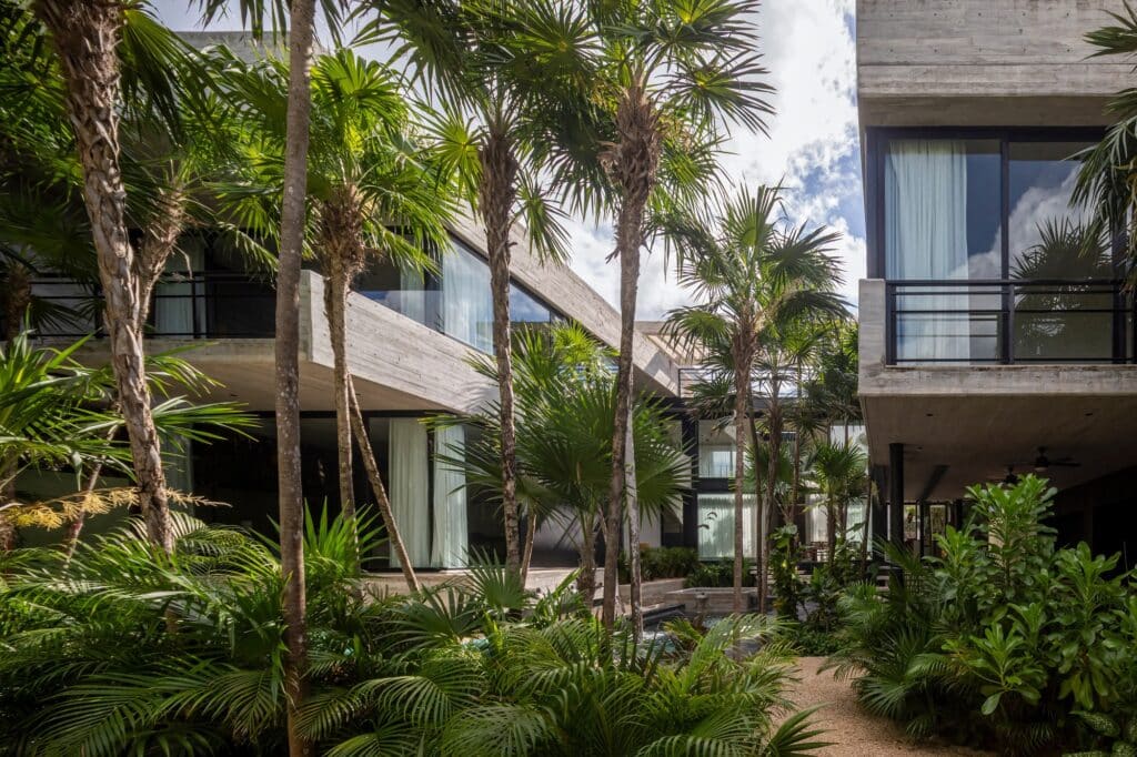 View from the tropical garden looking towards the tiered concrete balconies of Vihara House under a bright sky.