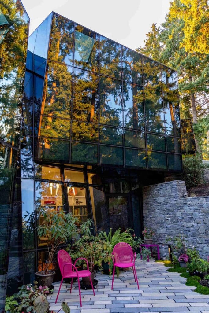 Close-up of a glass cantilevered volume reflecting tall pine trees, featuring a stone wall and terrace.