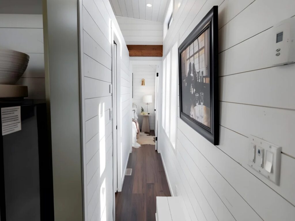 A bright interior hallway in the Daphne tiny house leading to the bedroom with white shiplap walls.
