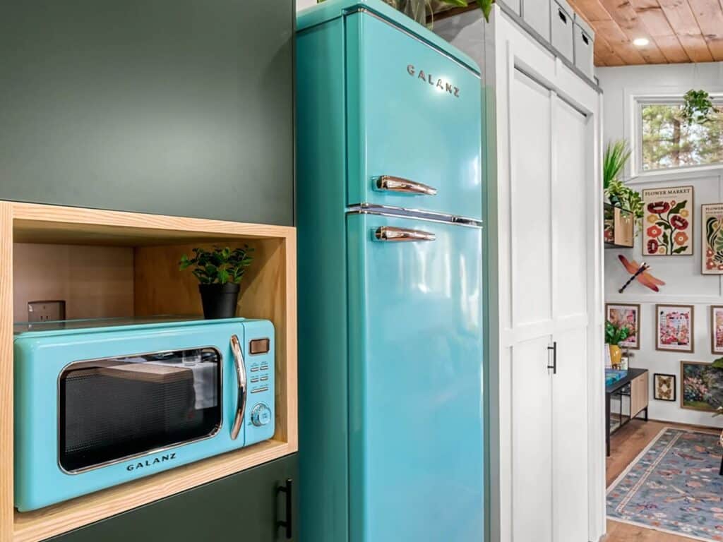 Turquoise retro-style Galanz refrigerator and microwave integrated into dark green kitchen cabinetry in a tiny home.