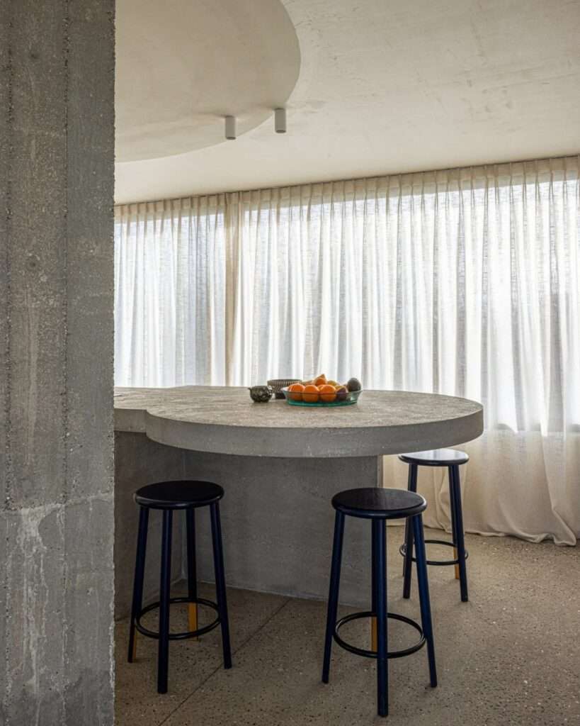 Detailed view of a concrete dining counter with minimalist black stools in a sunlit interior.