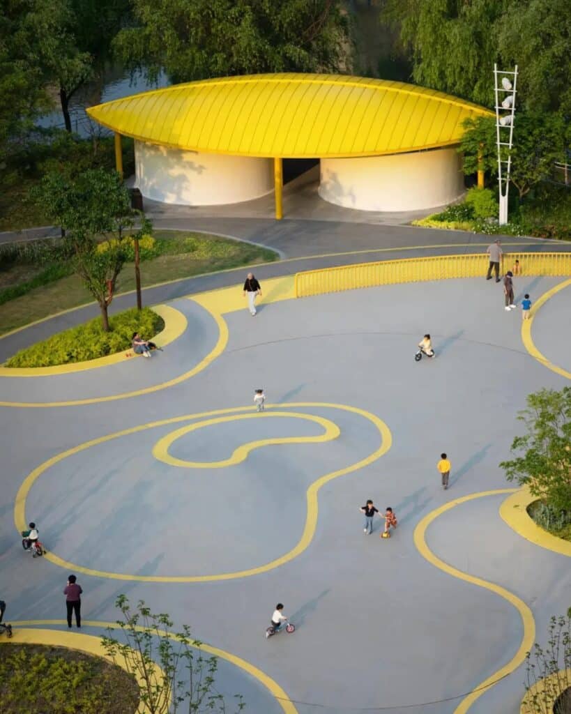 Wide shot of a grey paved activity area with yellow circular patterns and a large yellow pavilion in the background.