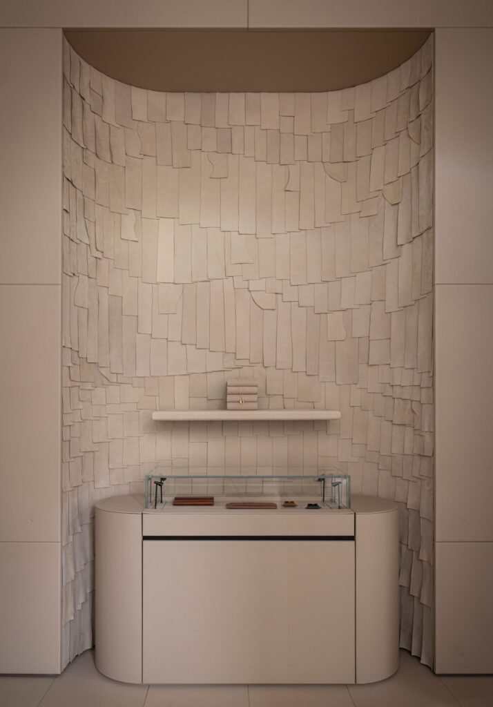 A curved wall niche covered in overlapping leather scales in a minimalist retail interior.