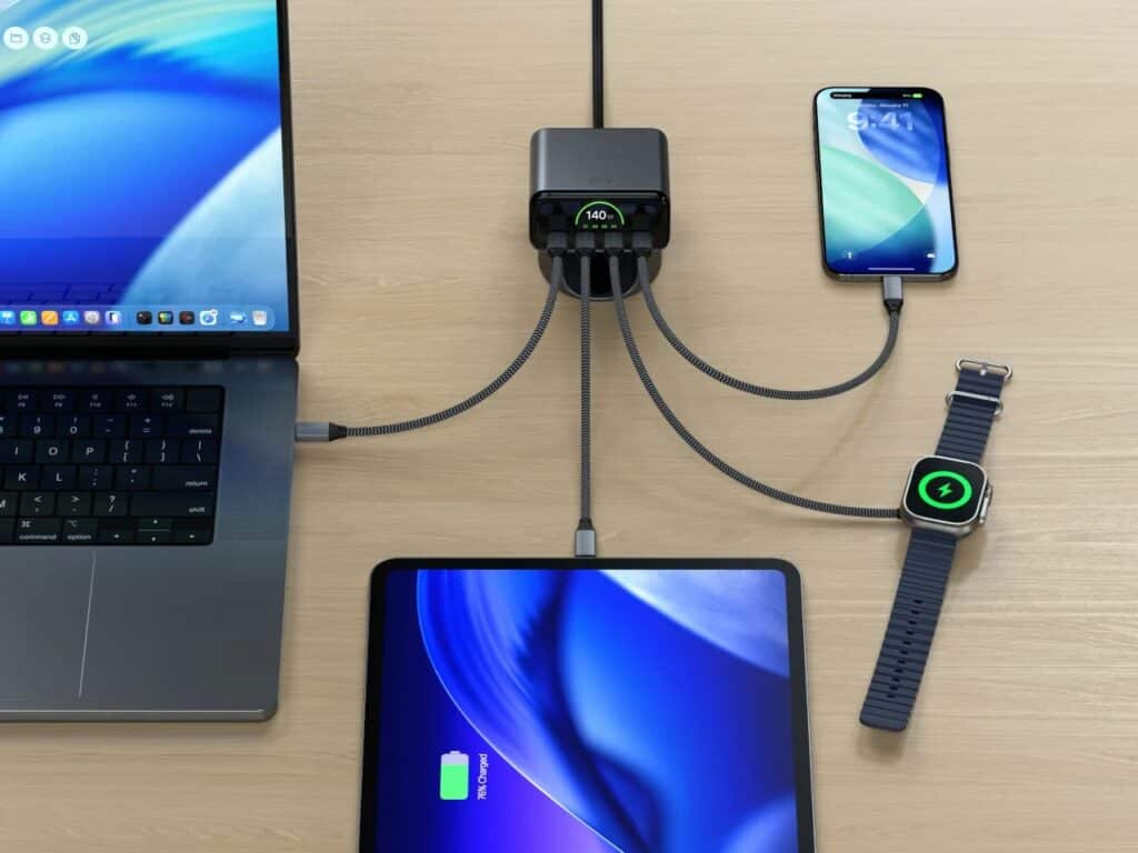 Top-down view of a workstation with Satechi ChargeView 140W charging a laptop, tablet, smartphone, and Apple Watch simultaneously.